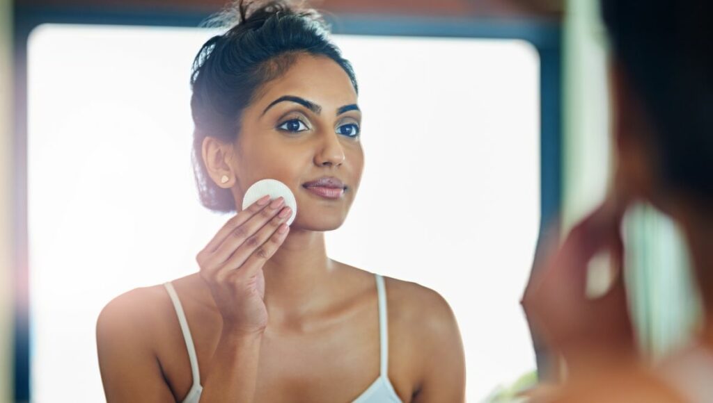 Femme appliquant un produit de soin sur son visage avec un coton visant à traiter les pores dilatés